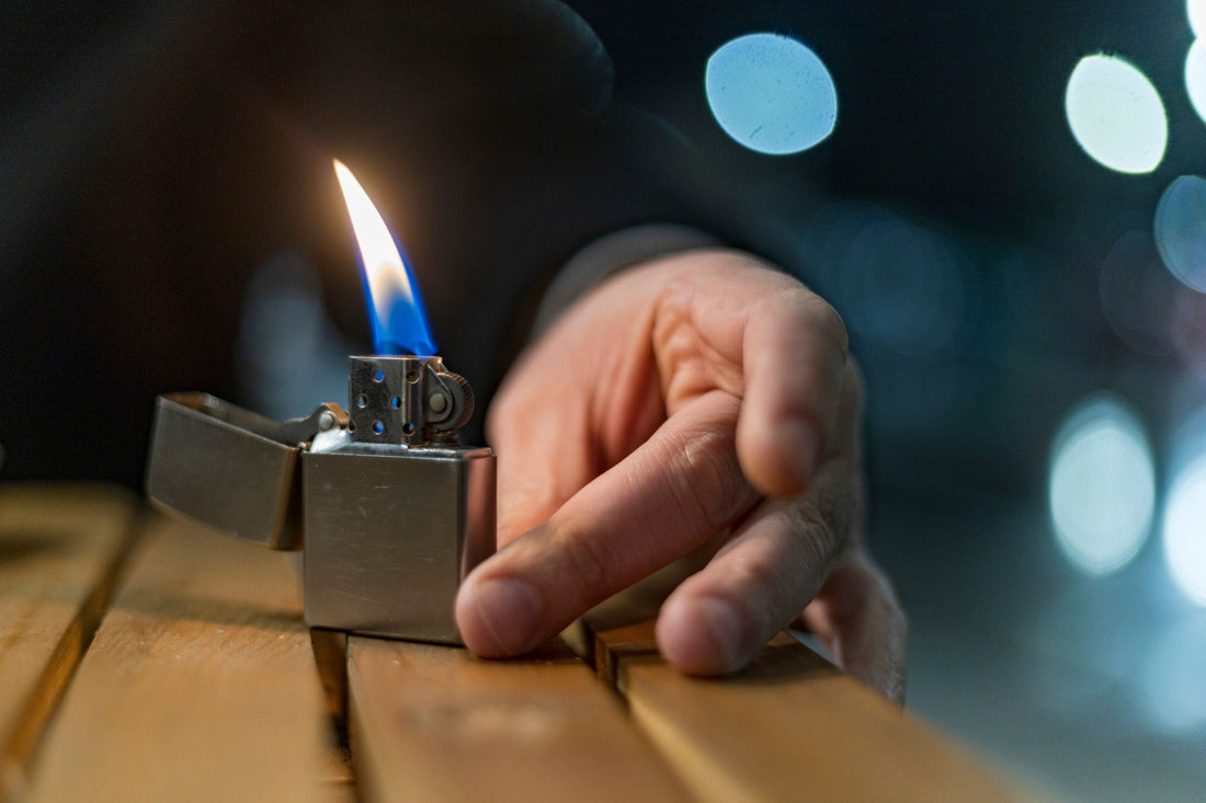 A detailed close-up of a hand lighting a metal lighter with a vibrant flame on a wooden surface.