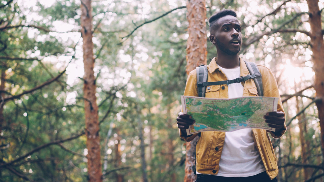 Young man with map hiking through a dense forest during the day.