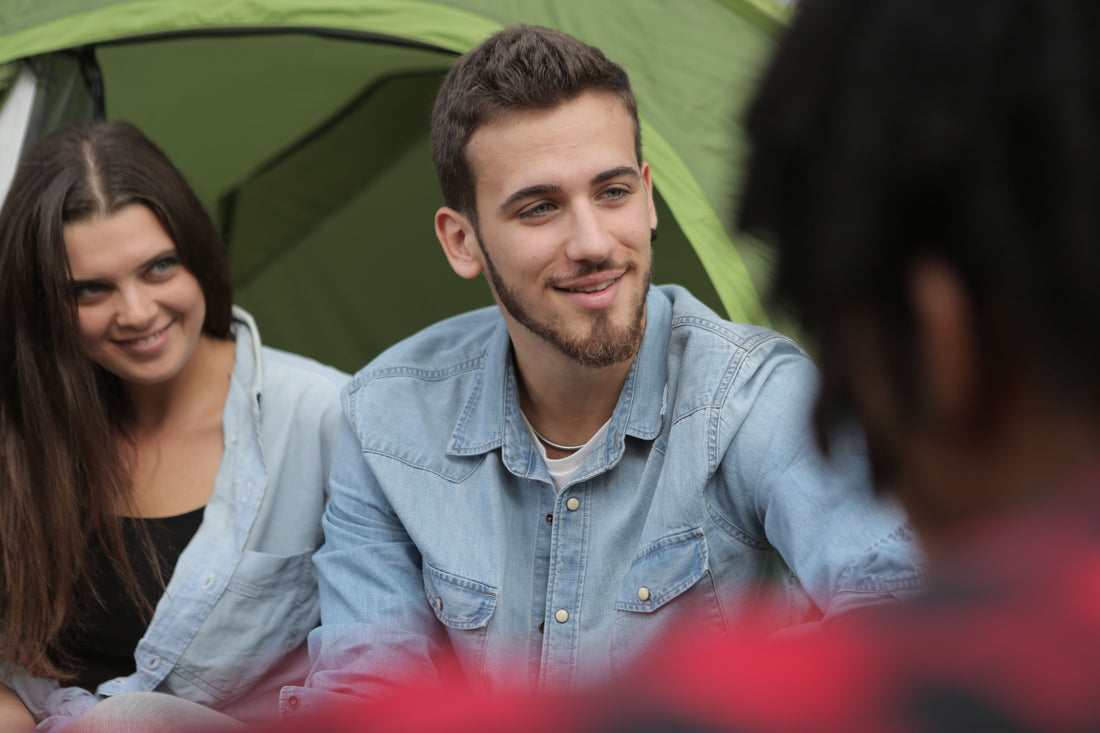 Cheerful couple in casual clothes sitting in company of friends while spending time together in camp
