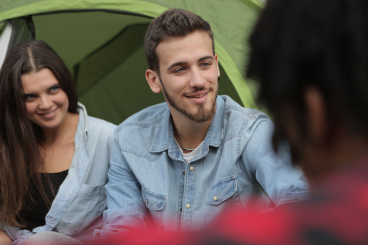 Cheerful couple in casual clothes sitting in company of friends while spending time together in camp