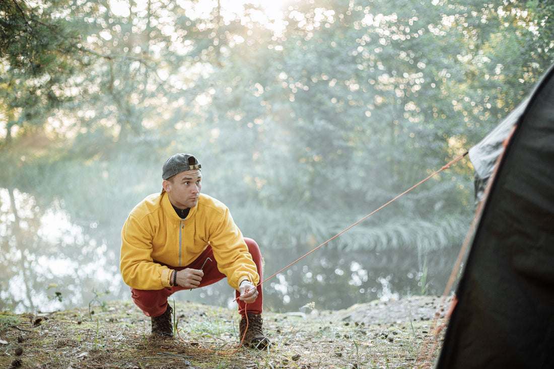 Young man setting up a tent at a campsite by the lake during early morning.